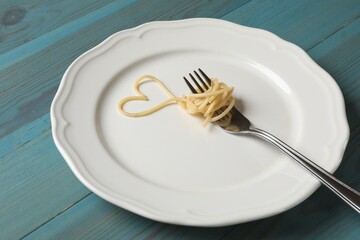 Heart made of tasty spaghetti and fork on light blue wooden table