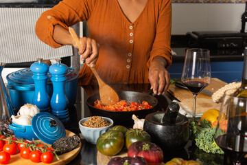 Close-up of a woman in an orange dress cooking at home kitchen. She is stirring a pan of sauteed...