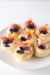 Delicious puff pastry with cream cheese, ham, black caviar and peach on white table