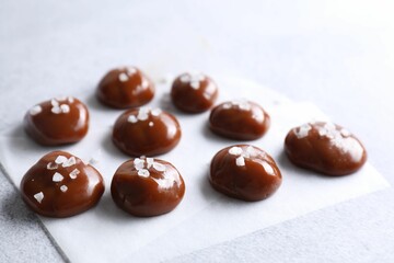Tasty caramel candies and salt on light grey table, closeup