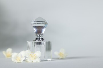 Aromatic perfume in bottle and beautiful jasmine flowers on grey background, space for text