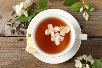 Aromatic jasmine tea in cup, flowers and dry leaves on wooden table, top view