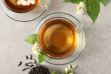 Aromatic jasmine tea in cups, flowers and dry leaves on light grey table, flat lay