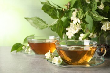 Aromatic jasmine tea in cups, flowers and green leaves on light grey table