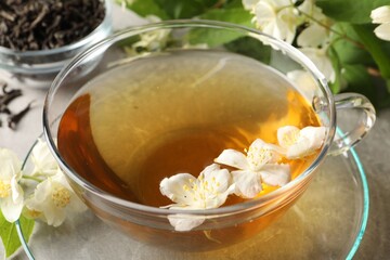Aromatic jasmine tea in cup, flowers and leaves on table, closeup