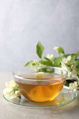 Aromatic jasmine tea in cup, flowers and green leaves on light grey table