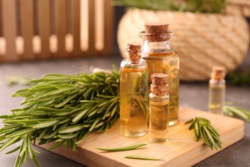 Essential oil in bottles and rosemary on grey table
