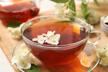 Hot jasmine tea in cup and flowers on white wooden table, closeup