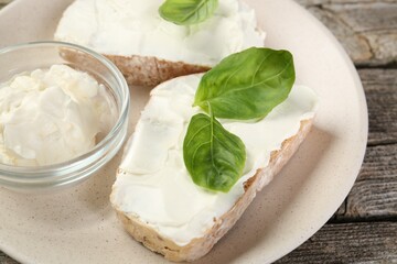 Delicious sandwiches with cream cheese and basil leaves on wooden table, closeup