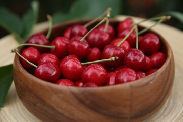 Tasty ripe red cherries in wooden bowl outdoors, closeup