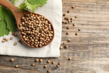 Spoon with dried coriander seeds and green leaves on wooden table, top view. Space for text