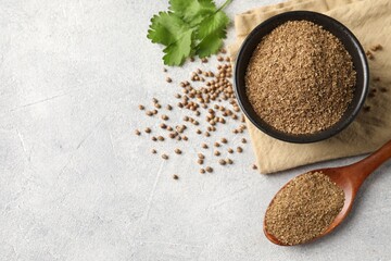 Coriander powder in bowl, spoon, seeds and green leaves on light grey table, top view. Space for text