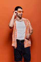 Handsome man in trendy attire, wearing white t-shirt and orange cardigan.