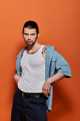 Fototapeta premium A stylish Caucasian man standing confidently in front of a bright orange wall.