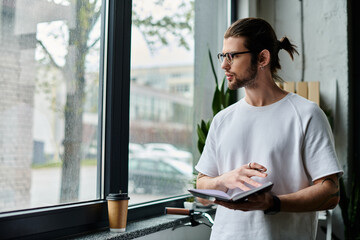A man holding a book, standing in front of a window.