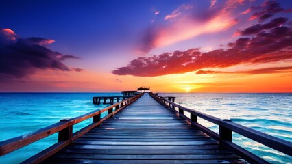Obraz premium A scenic view of the sunset over the ocean. The sky changes color from purple to orange, and a wooden walkway stretches from the foreground to the horizon. 