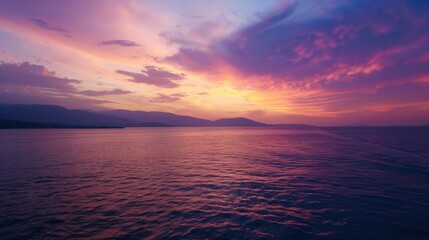Fototapeta premium A sunset over a calm sea, with the sky filled with pink, purple, and orange hues, and mountains visible in the distance.