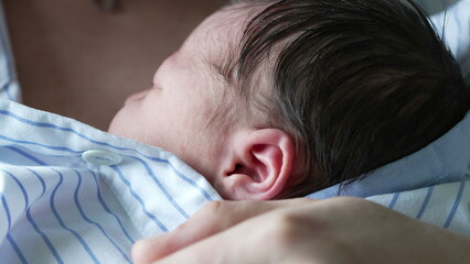 Close-up of a newborn baby sleeping on the mother's chest, wrapped in a blue and white striped...
