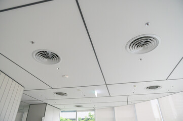 A clean, modern office ceiling featuring air vents, recessed lighting, and a grid pattern.