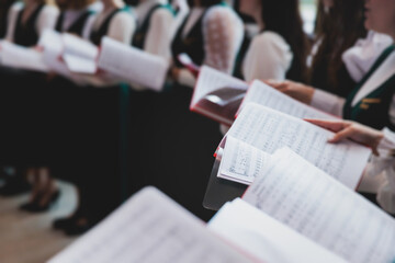 Church choir concert in cathedral, choral artists singing, group of European boys and girls singing in a chorus, students and choristers in white and green uniform performing on stage with conductor