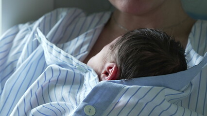 Mother holding her newborn baby close to her chest in a hospital room. The baby, wrapped in a...