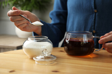 Woman adding sugar into aromatic tea at wooden table indoors, closeup
