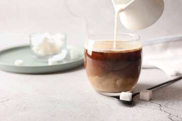Pouring milk into cup with coffee on white textured table, closeup