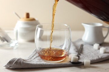 Pouring warm tea into cup on white wooden table, closeup