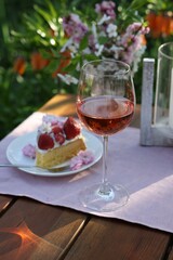 Vase with spring flowers, wine and cake on table served for romantic date in garden