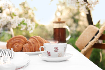 Stylish table setting with tea and croissants in spring garden