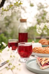 Stylish table setting with beautiful spring flowers, fruit drink and pie in garden