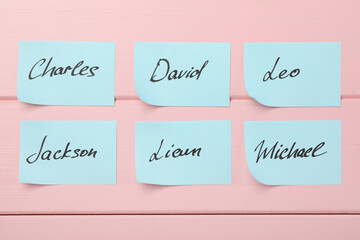 Paper stickers with different names on pink wooden background, flat lay. Choosing baby's name