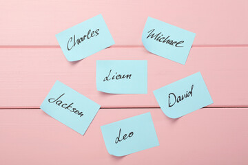 Paper stickers with different names on pink wooden background, flat lay. Choosing baby's name