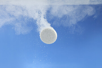 Effervescent pill dissolving in water on blue background, closeup
