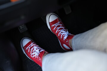 Woman in sneakers pushing on pedal of car brake, closeup
