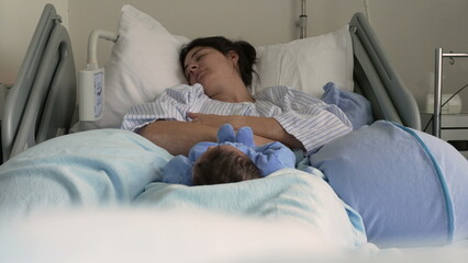 Mother and newborn baby resting together in a hospital bed. The baby, in a blue onesie, lies on a soft blanket, capturing the serene atmosphere and tender bonding moments post-birth