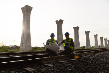 Two male railway technicians are actively reviewing blueprint drawings and meticulously inspecting...