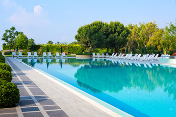Resort hotel swimming pool with white lounge chairs and umbrellas; copy space