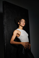 Fototapeta premium A stylish young woman in a white tank top poses against a grey background.