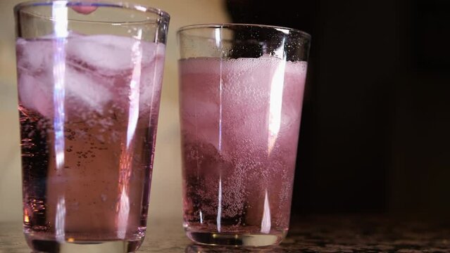 Slow motion pour pink fizzy drink in a tumbler glass on concrete countertop with window . Pink fizzy drink