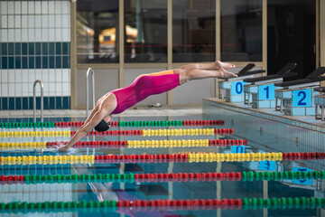Female athlete, a professional swimmer during training, preparing for a dive start and jumping into the lap pool.