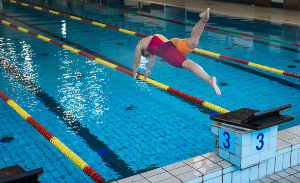 Female athlete, a professional swimmer during training, preparing for a dive start and jumping into the lap pool.