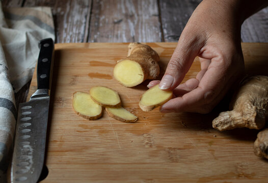 Concept of taking or grabbing food with hands, feminine Mexican hands. Slices of jinger. slices of ginger on a wooden cutting board over a rustic wood table