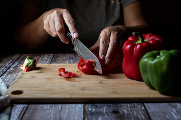 Concept of taking or grabbing food with hands, feminine Mexican hands. Cutting peppers in slices on a wooden cutting board. horizontal front view dark mood image 