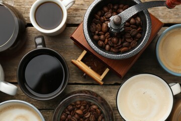 Different coffee drinks in cups, beans and manual grinder on wooden table, flat lay
