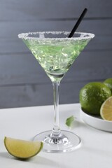 Delicious Margarita cocktail with ice cubes in glass and lime on white table
