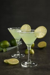 Delicious Margarita cocktail in glasses and limes on grey table