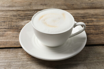 Tasty cappuccino in coffee cup on wooden table, closeup
