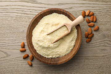 Fresh almond flour in bowl, scoop and nuts on wooden table, top view