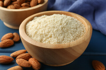 Fresh almond flour in bowl and nuts on blue wooden table, closeup